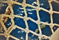 Blick durch ein grobes, geknotetes Netz auf eine entfernte Wasseroberfläche